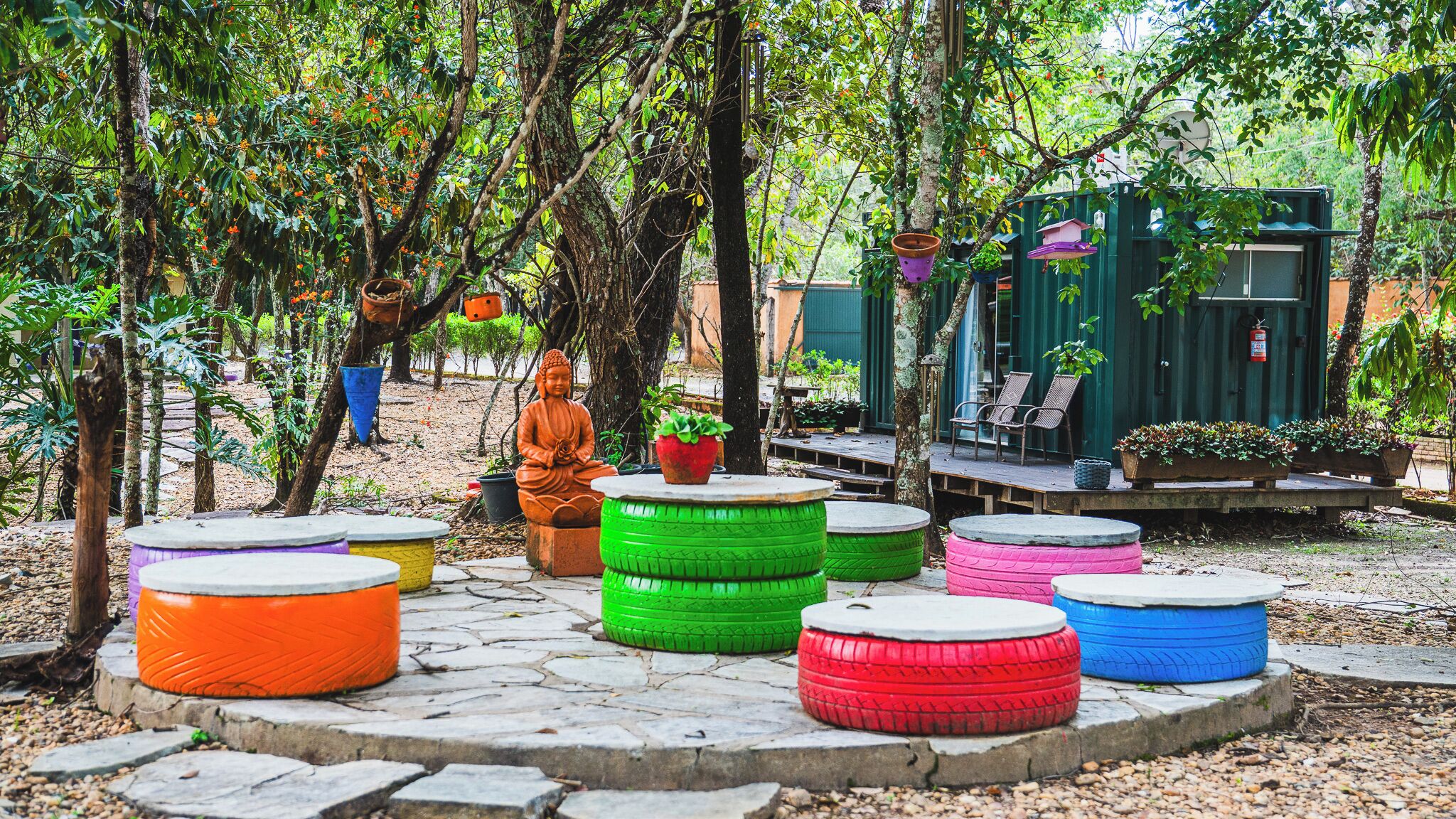 A serene outdoor setting with a Buddha statue, colorful tire seating, and a rustic wooden structure.