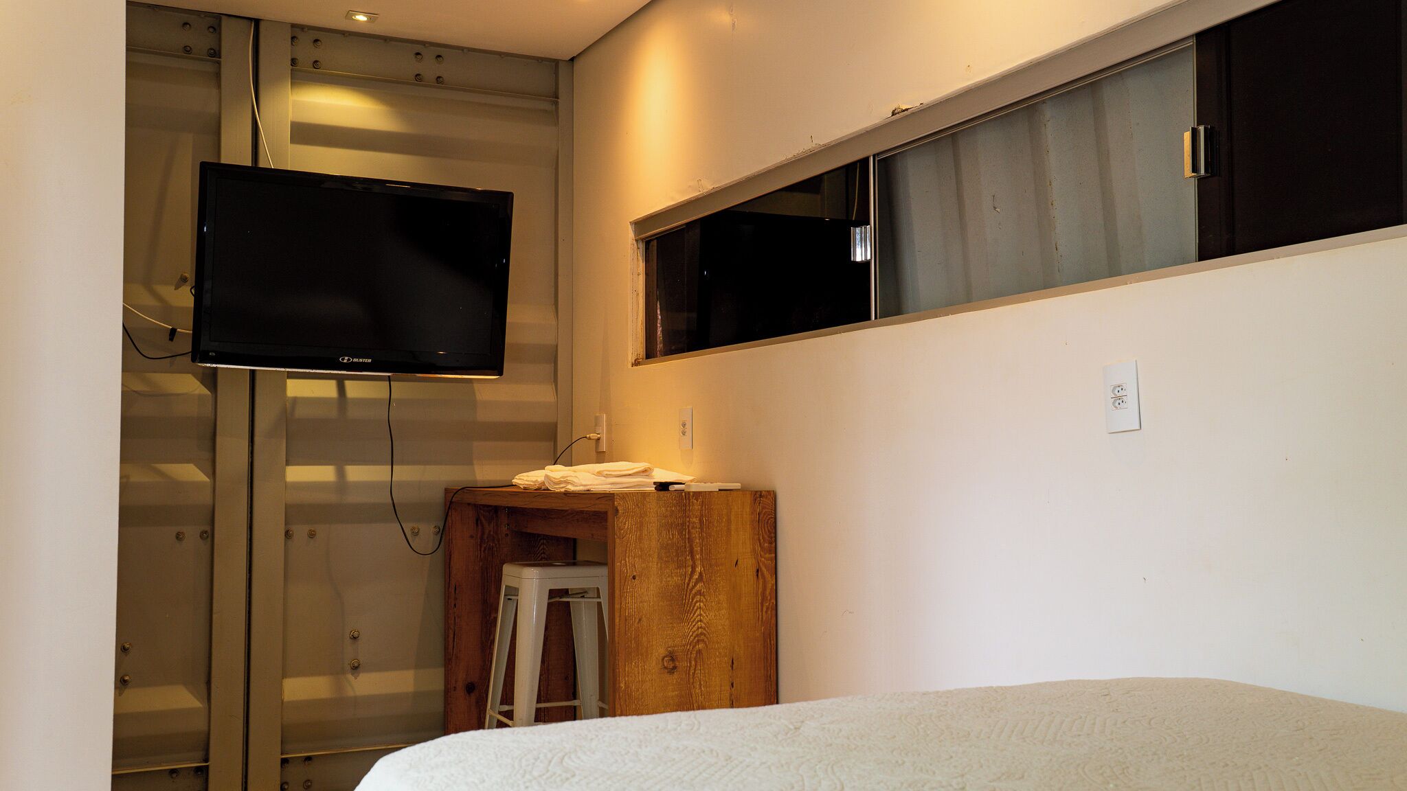 A bedroom with a bed, a wooden nightstand, a TV mounted on a wall, and a window.