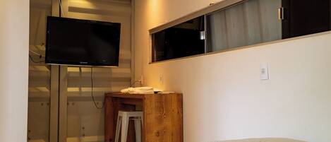 Une chambre à coucher avec un lit, une table de chevet en bois, un téléviseur fixé au mur et une fenêtre.