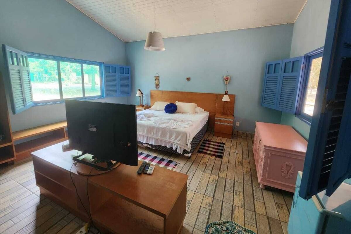 A bedroom with a bed, a desk with a computer, a dresser, and a window with shutters.