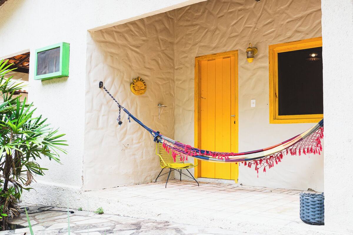 A white building with a yellow door, a hammock, and a chair outside.