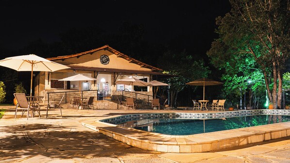 Un área junto a la piscina con mobiliario exterior y un edificio con tejado de azulejos.