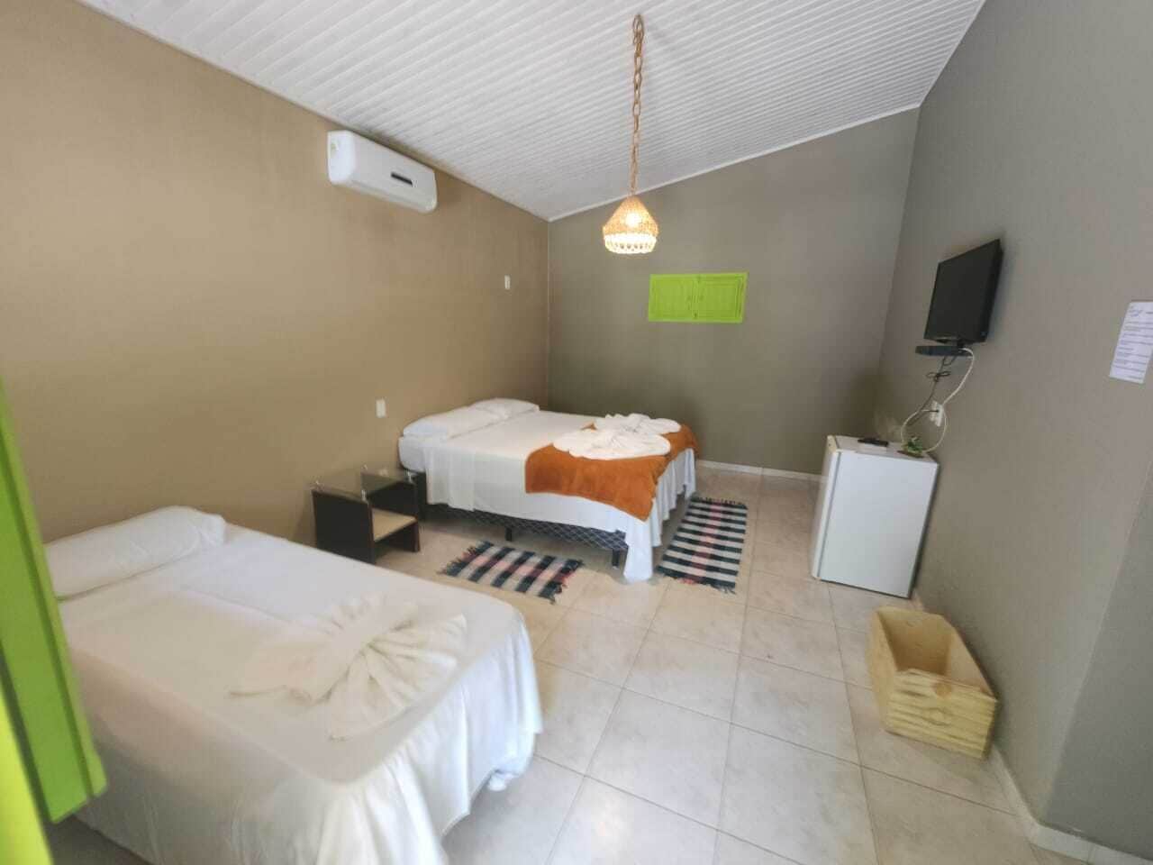 Habitación de hotel con dos camas individuales, un escritorio, un refrigerador pequeño, televisión y una lámpara colgante.