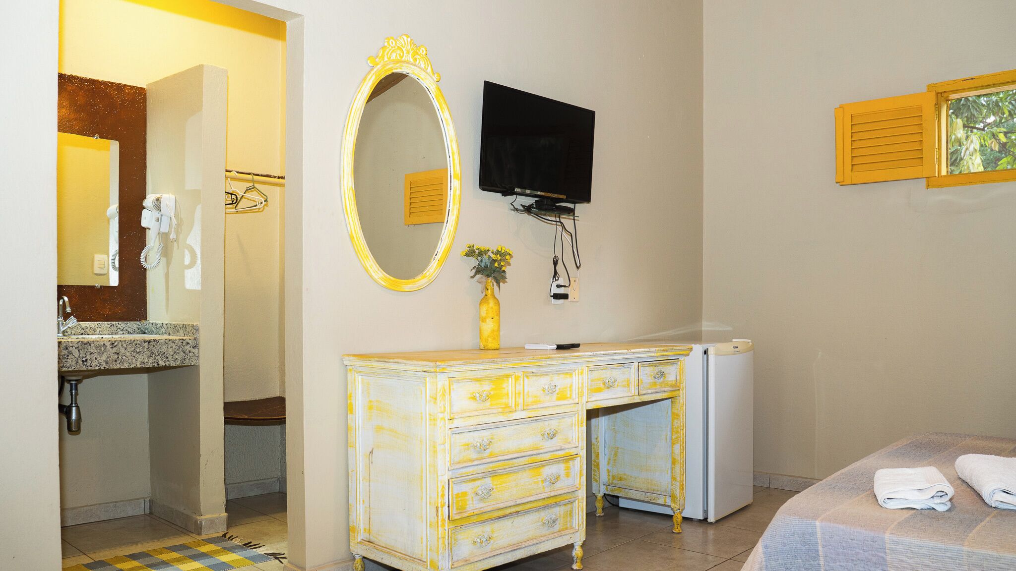 A hotel room with a bed, a dresser, a mirror, a TV, and a small refrigerator.