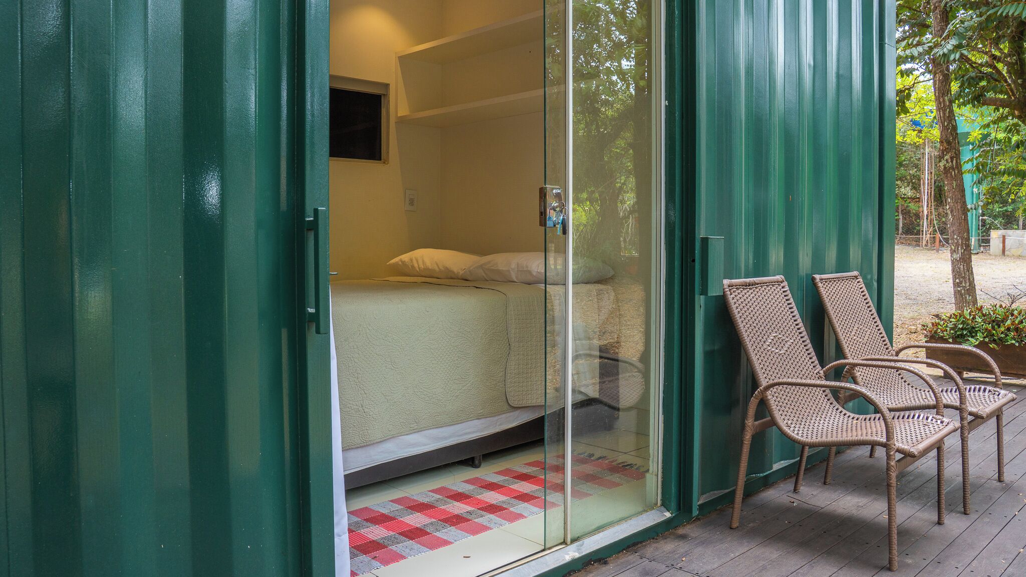 A room with a bed, a glass door, and two wicker chairs outside.