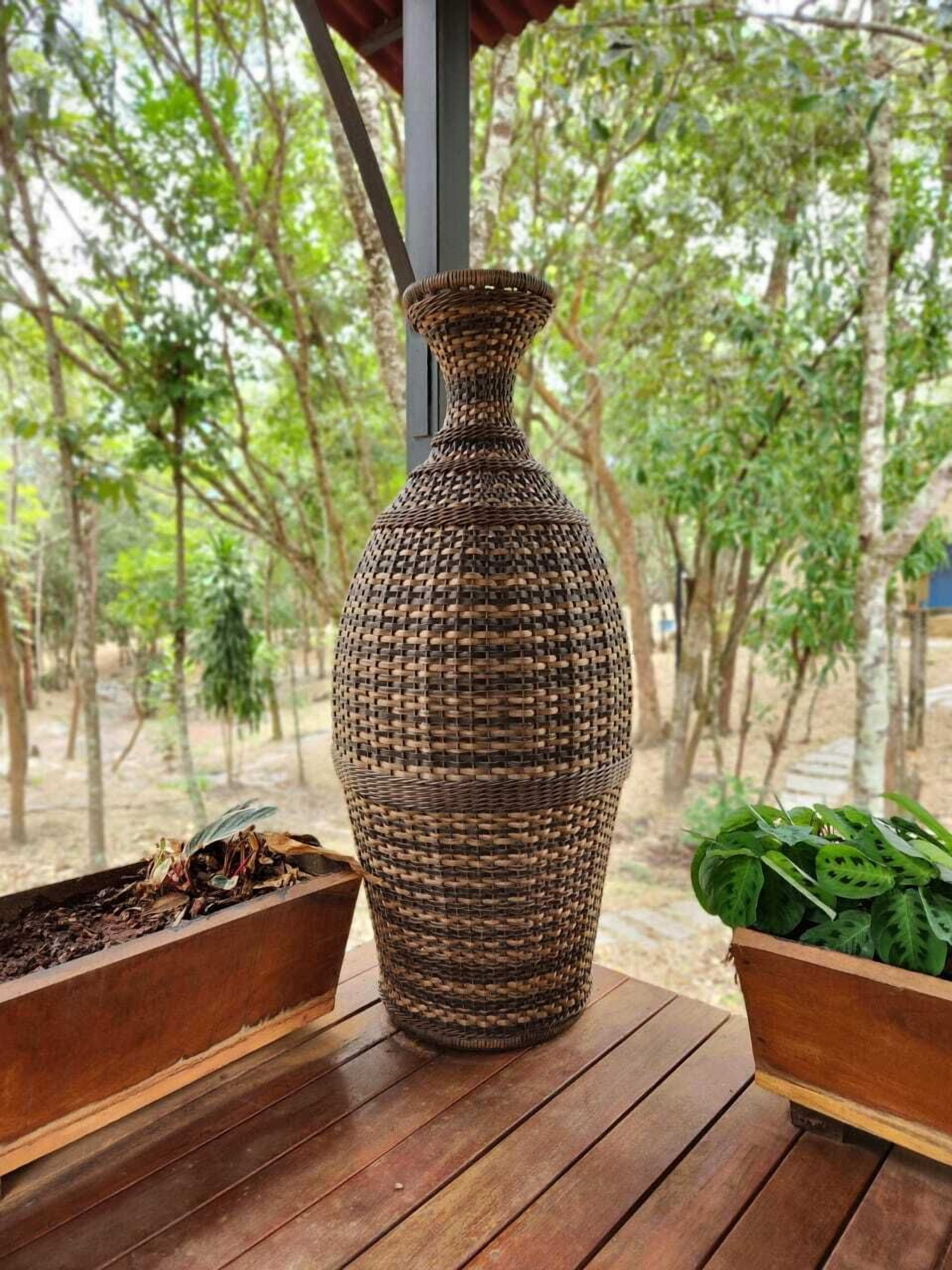 A wicker vase on a wooden table with a view of trees.