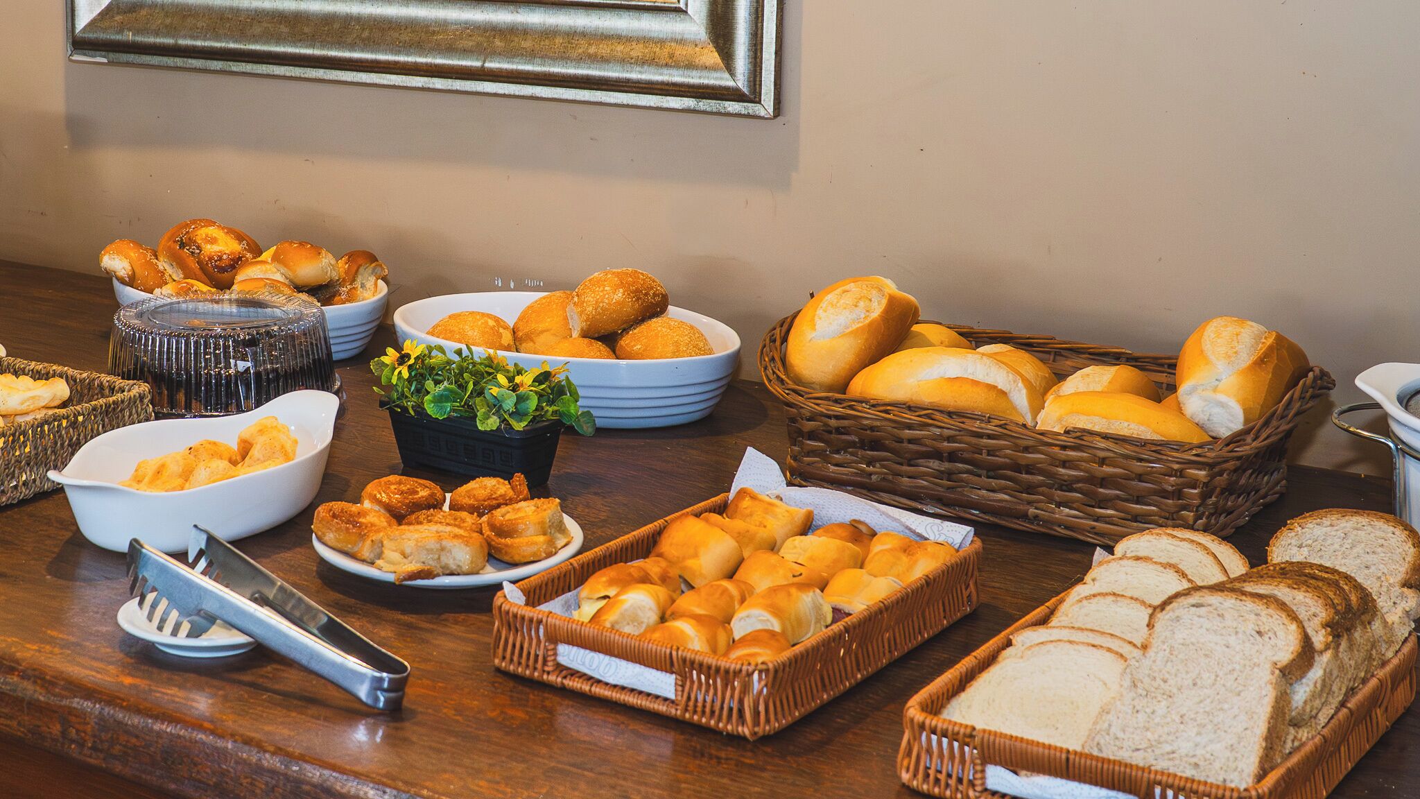 A buffet table with various baked goods, including bread rolls, pastries, and sliced bread.