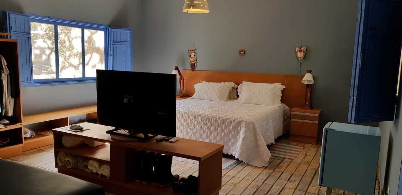 A bedroom with a bed, a TV, a wooden table, and a window.