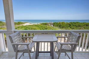A balcony with two wooden chairs and a small table, overlooking a beach with a wooden walkway and greenery. - BEACHFRONT Beauty in the Dunes!!, 5BR/4BA, (St. George Island)