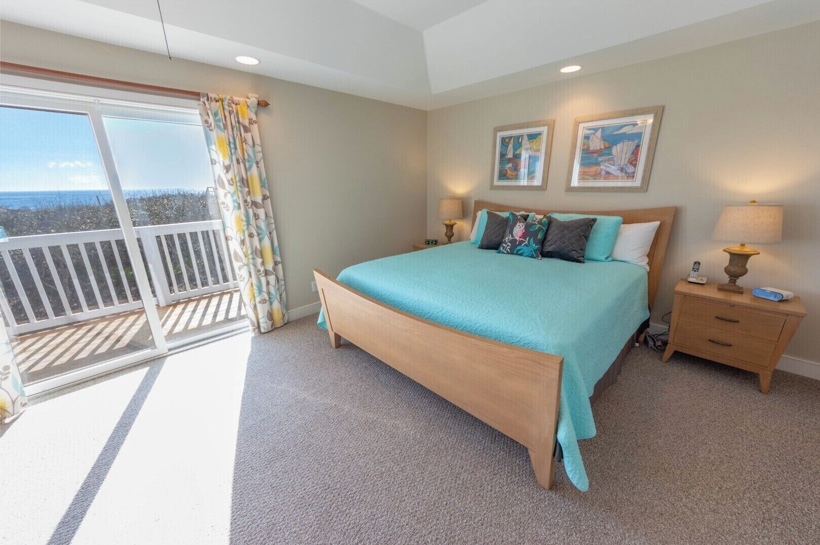 A bedroom with a bed, a nightstand, a lamp, and a view of the outdoors through a balcony.
