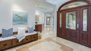 A hallway with a bench, a large wooden door with glass panels, and a painting of a sea turtle. - Ohana Kamalani: Lavish Fairwayfront Home w/Pool, AC & Stunning Sunsets! (Princeville)
