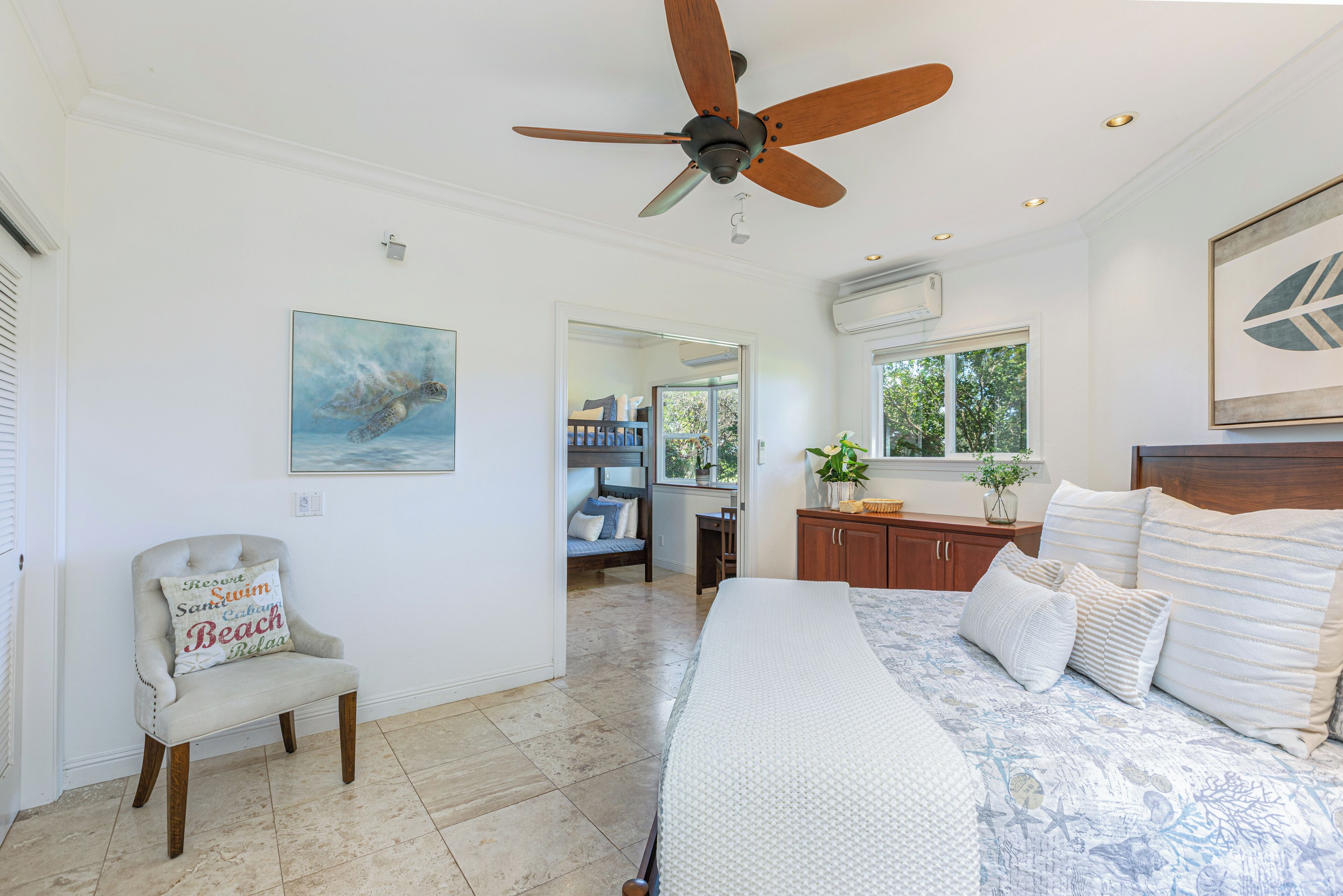 A bedroom with a bed, a ceiling fan, a chair, and a painting on the wall.