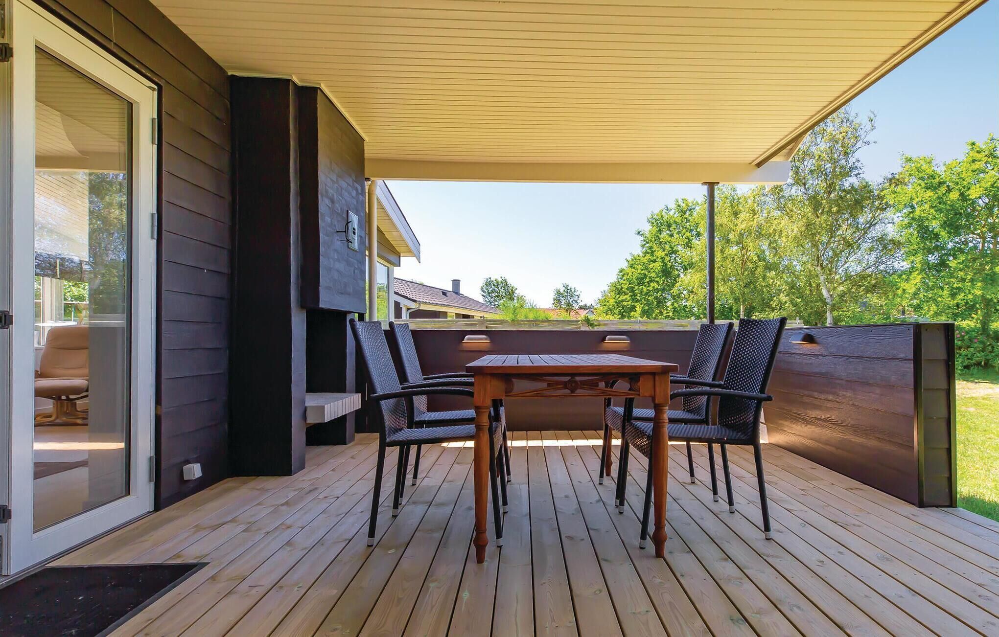 A covered outdoor patio with a wooden table and chairs, a sliding glass door, and a view of a house and trees.