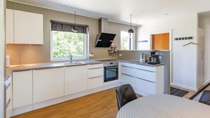 Een moderne keuken met witte kasten, een ingebouwde oven, een spoelbak en een raam met uitzicht op groen.