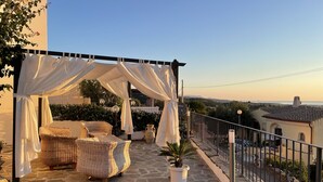 A stone-floored outdoor seating area with a wicker sofa and a potted plant, under a white canopy. - Vacation home with sea view, Budoni - Sardinia  (Solitá)