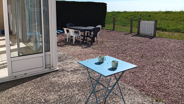 A covered outdoor seating area with a table and chairs, a small table with two cups, and a gravel ground.