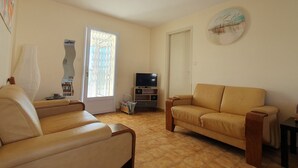 A living room with two sofas, a television, and a window with patterned curtains.