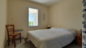 A bedroom with a bed, a chair, a nightstand, a lamp, a window, and a wall clock.