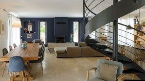 A modern living room with a wooden dining table, a sofa, and a spiral staircase. - Bastide Blanche: Villa with swimming pool and pétanque court in Lourmarin. (lourmarin)