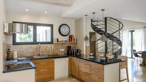 A modern kitchen with a central island, wooden cabinets, a built-in dishwasher, and a black spiral staircase leading to an upper level. - Bastide Blanche: Villa with swimming pool and pétanque court in Lourmarin. (lourmarin)