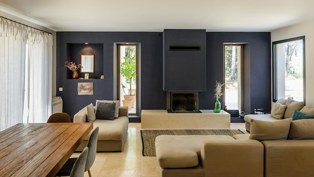 A modern living room with a wooden dining table, beige sofas, a fireplace, and large windows. - Bastide Blanche: Villa with swimming pool and pétanque court in Lourmarin. (lourmarin)