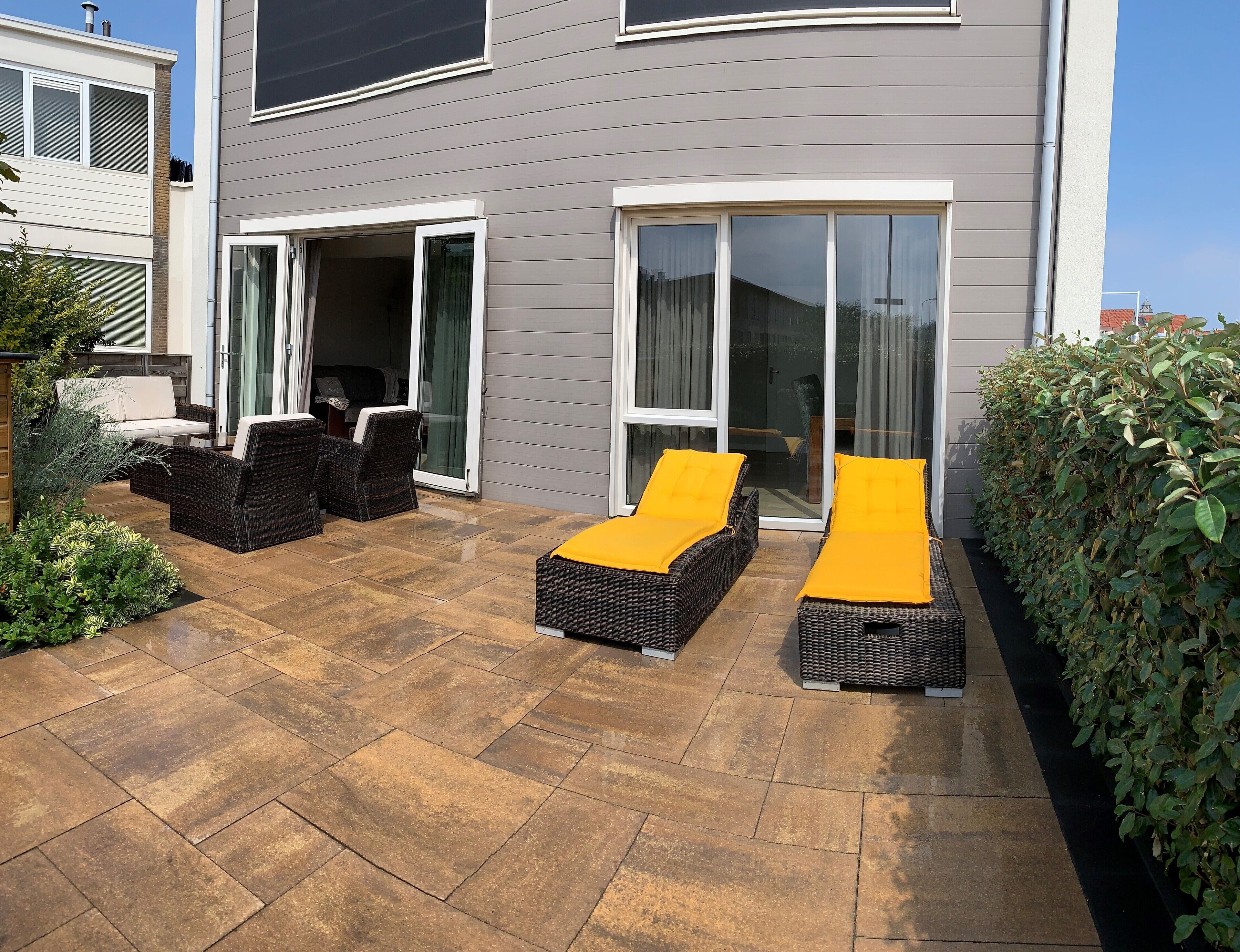 A patio with two wicker lounge chairs with yellow cushions, a white sofa, and a glass door leading to an interior space.