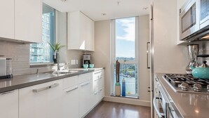 Eine moderne Küche mit einem großen Fenster, Edelstahlgeräten und Blick auf eine Stadtlandschaft.