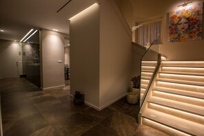 Un intérieur moderne avec un escalier, un ascenseur en verre et un couloir doté d’un sol carrelé.