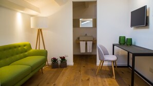 Une chambre moderne avec un canapé vert, un bureau avec une chaise, une télévision, un miroir et une lucarne.
