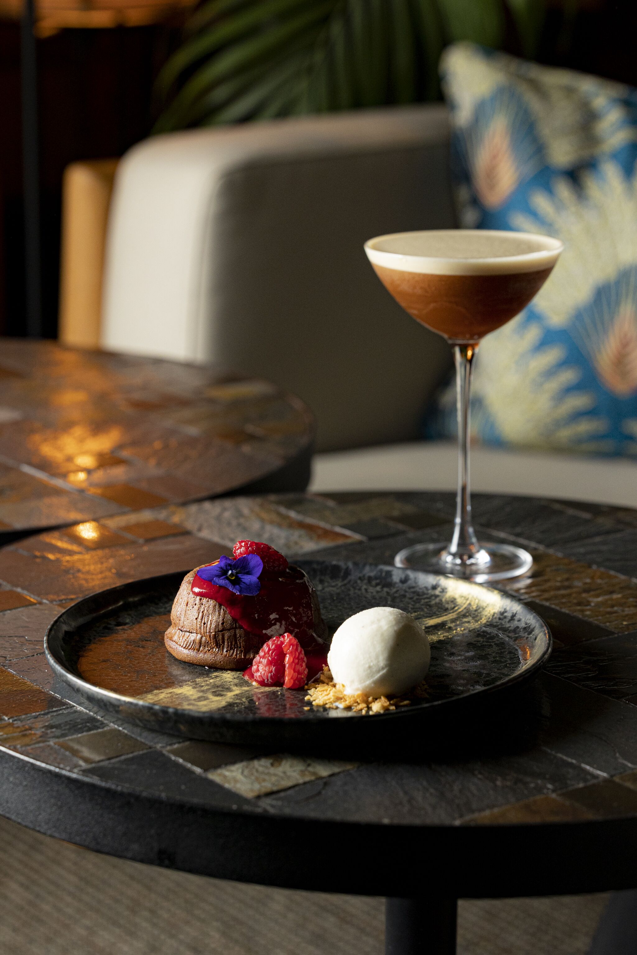Un plato de postre con un dulce de chocolate, una porción de helado y una copa de martini sobre una mesa de baldosas.