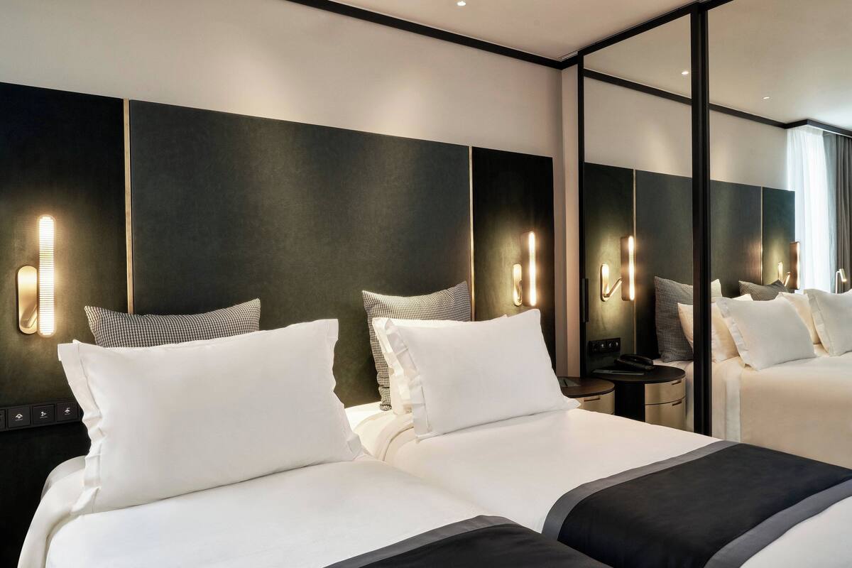 A hotel room with two beds, a large mirror, and wall-mounted lighting.