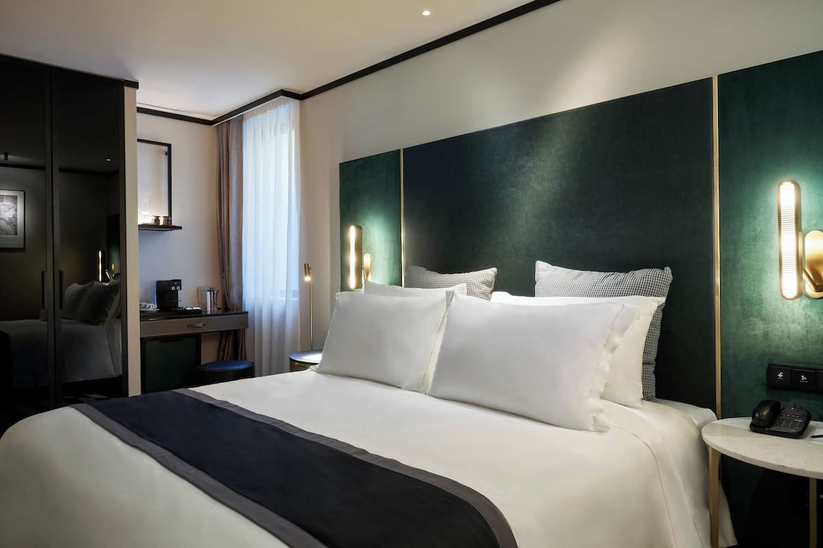 A hotel room with a large bed, bedside tables, a desk with a chair, and a large window with curtains.