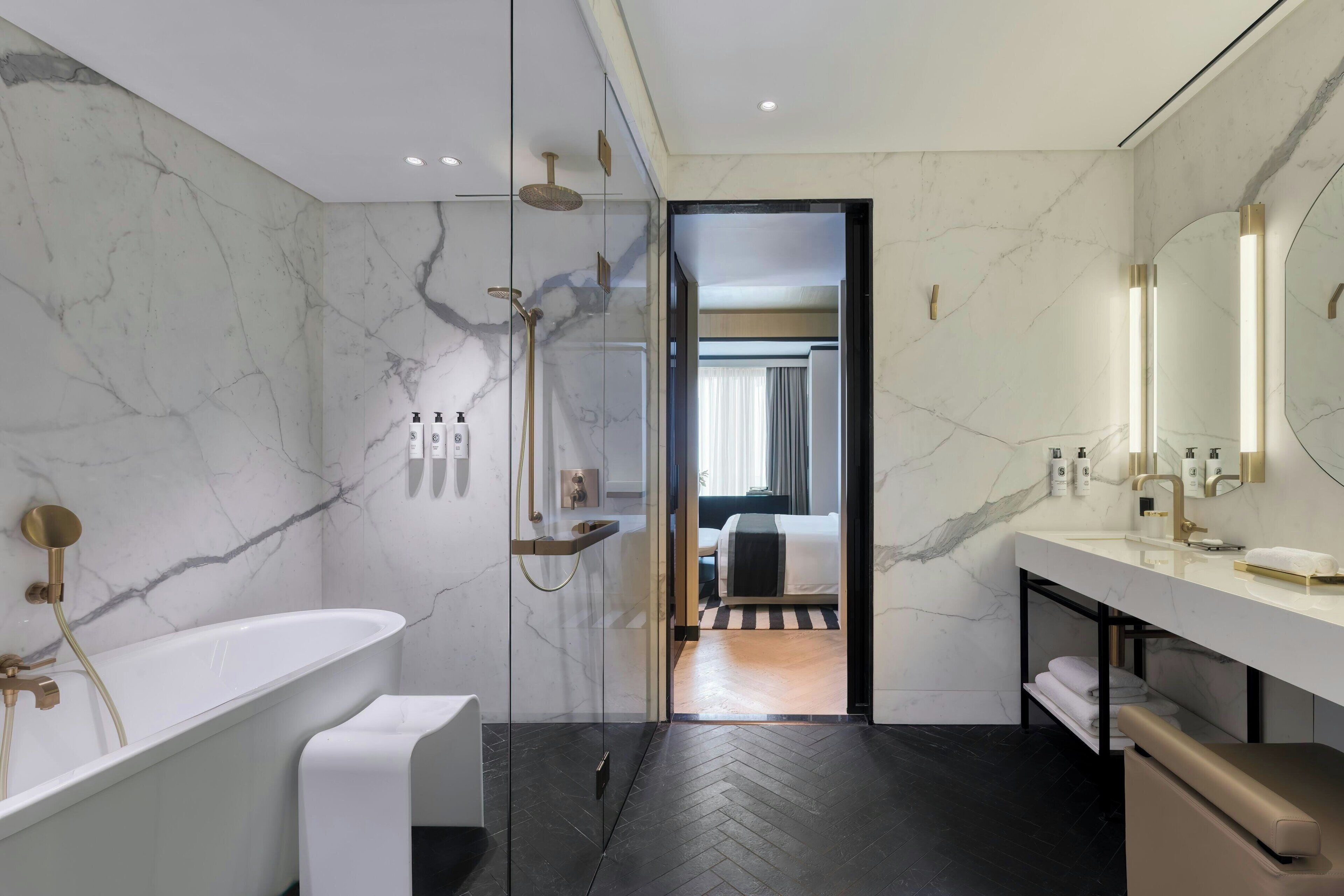 Une salle de bain moderne avec un mur en marbre, une baignoire sur pieds, une douche à parois de verre et un meuble-lavabo avec un miroir.