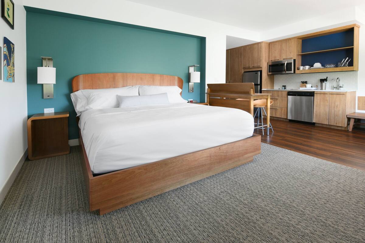 Quarto de hotel moderno com cama de madeira, pequeno-almoço e uma parede de destaque azul-esverdeado.