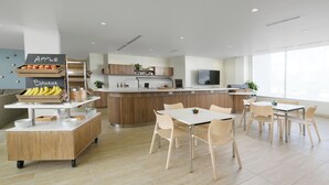 Una cocina moderna con una isla central, un área de comedor con sillas de colores claros y una barra americana con frutas y verduras frescas.