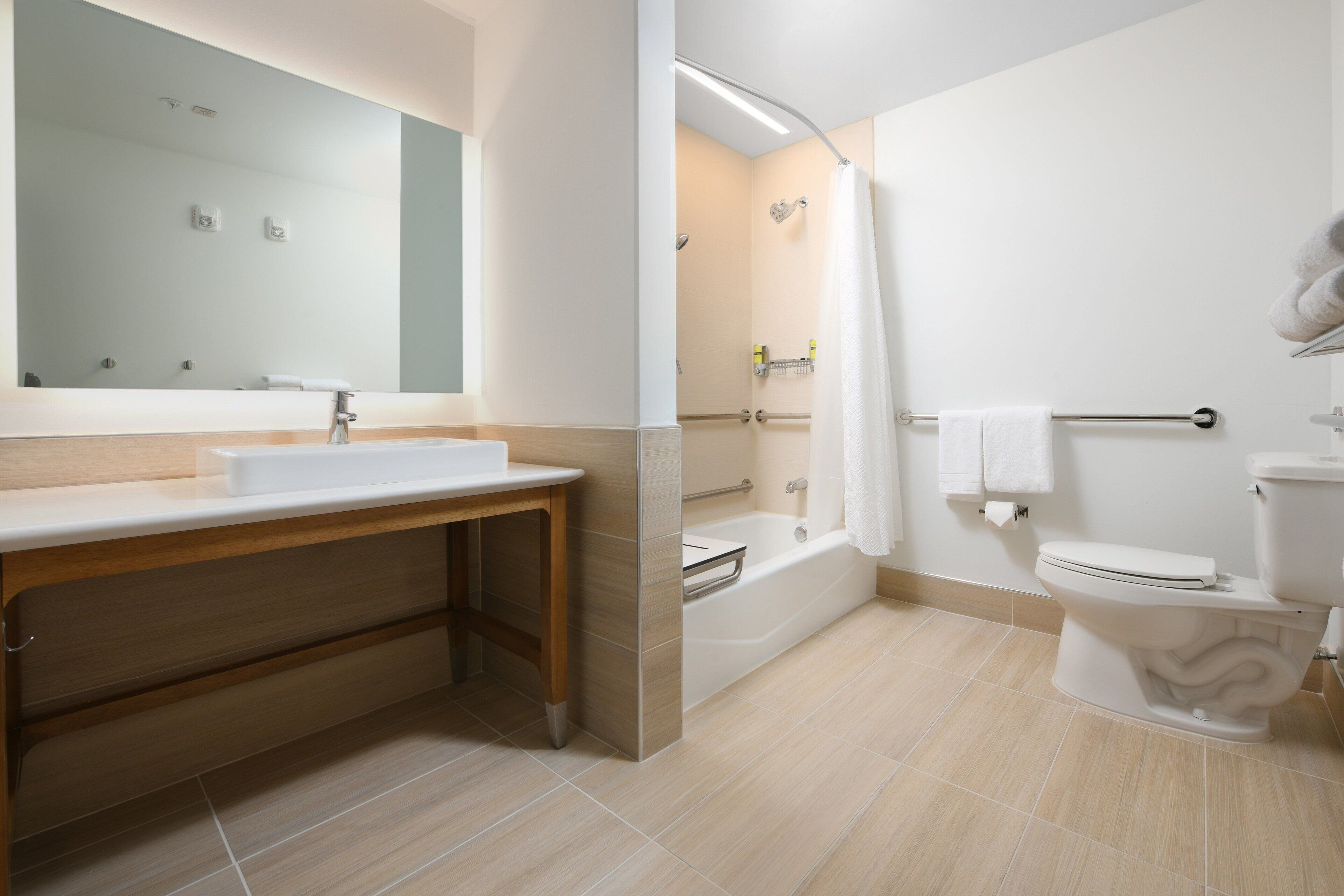 A modern bathroom with a sink, mirror, bathtub, and toilet.