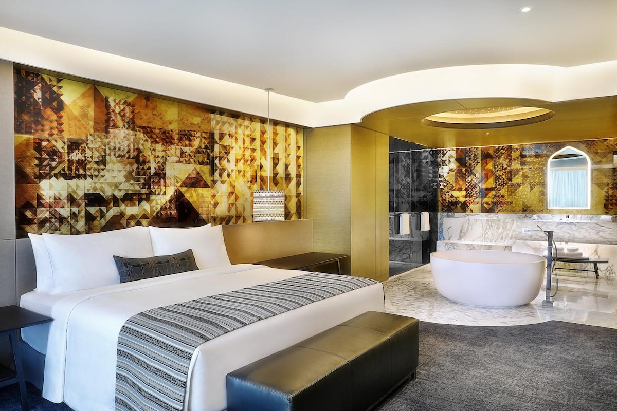 A modern hotel room with a large bed, a bathtub, and a bathroom with a marble countertop.