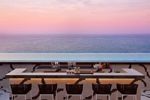 A bar with a view of the ocean, featuring a tiled floor and black chairs.