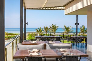 A terrace with tables set for dining, overlooking a beach with palm trees and the ocean.