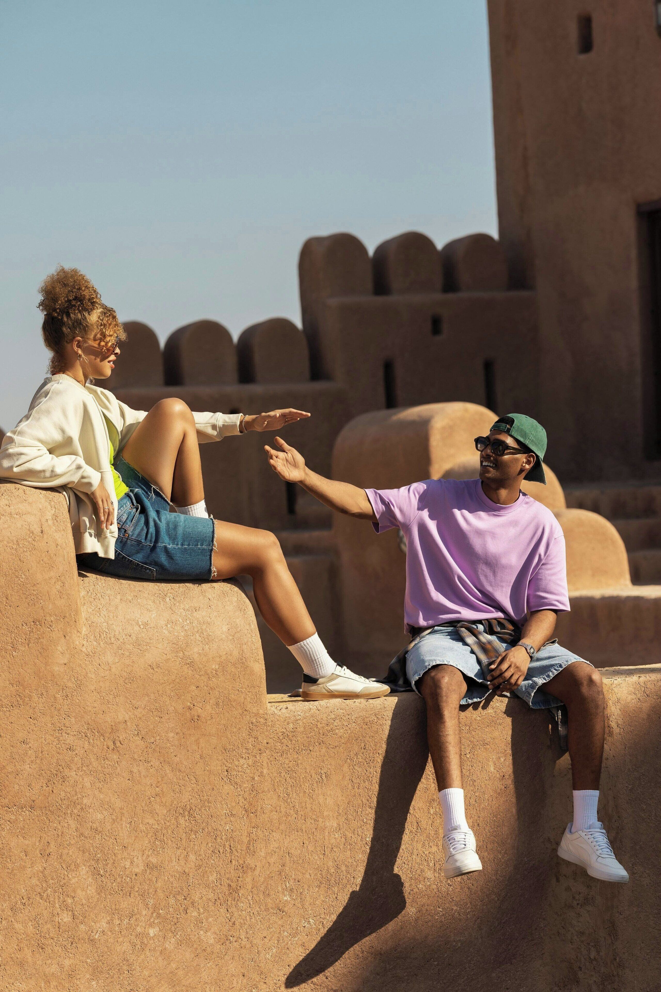 Two people sitting on a stone wall with a large building in the background.