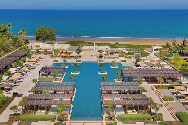 A resort with a central pool, multiple lounge areas, and a beach view.