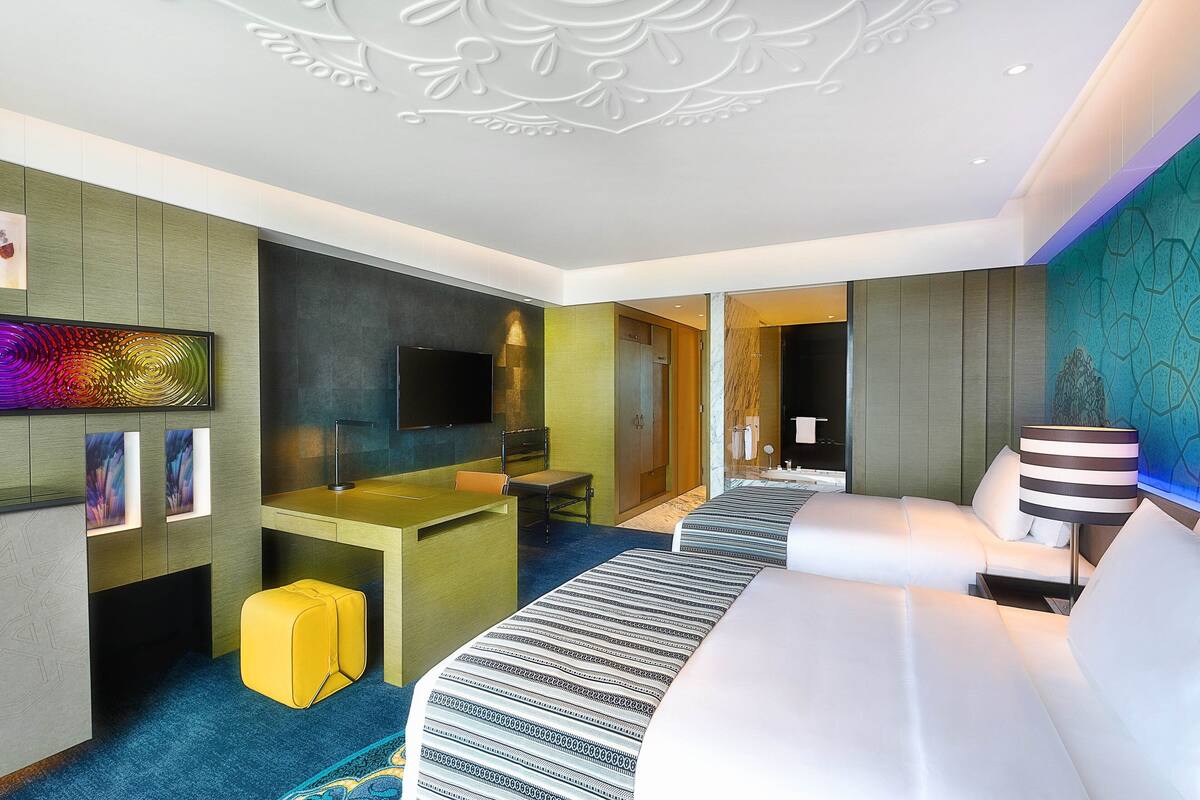 A modern hotel room with a flat-screen TV, a desk, a sofa, and a bed.