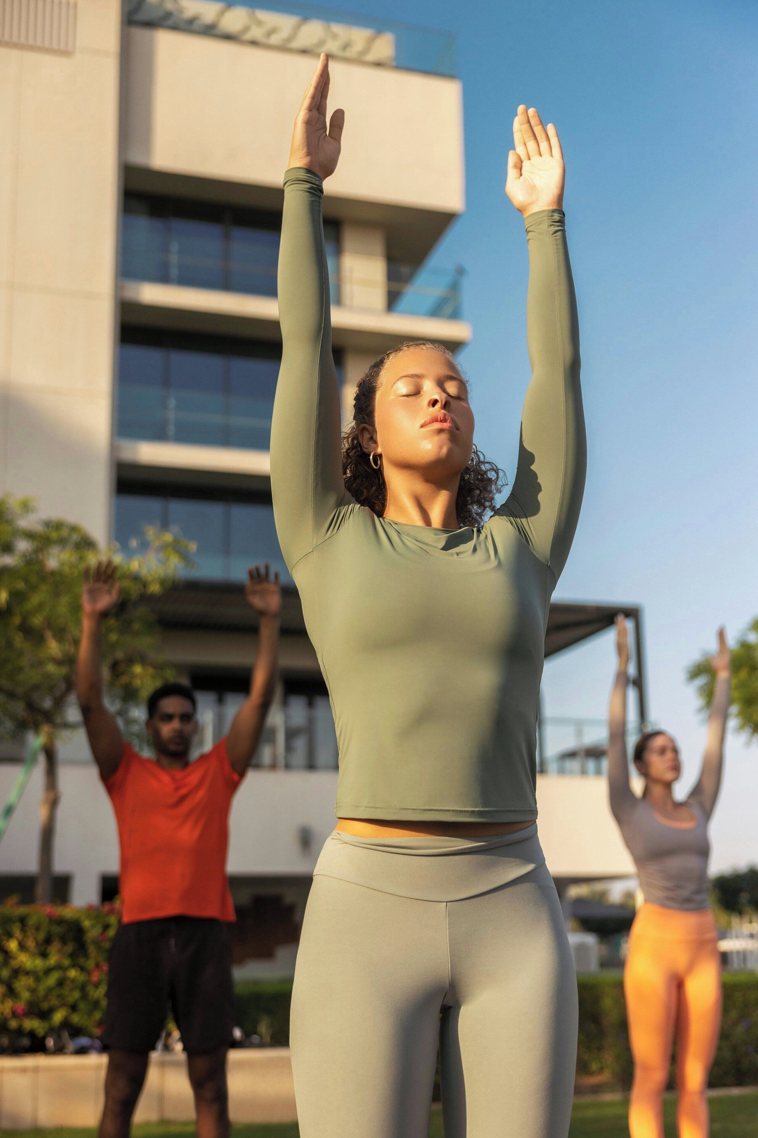A person in a green top and leggings performing an exercise with arms raised.