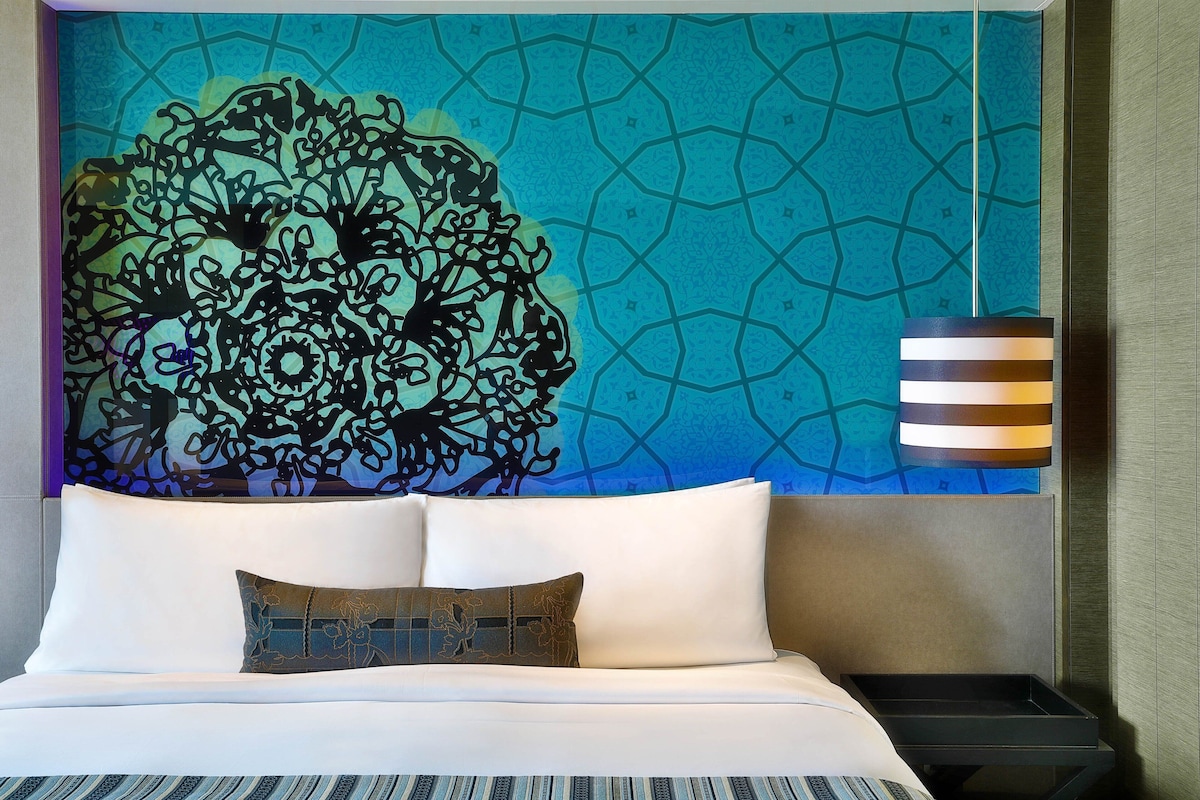 Habitación de hotel con cama, un adorno en la pared y una mesita de noche.