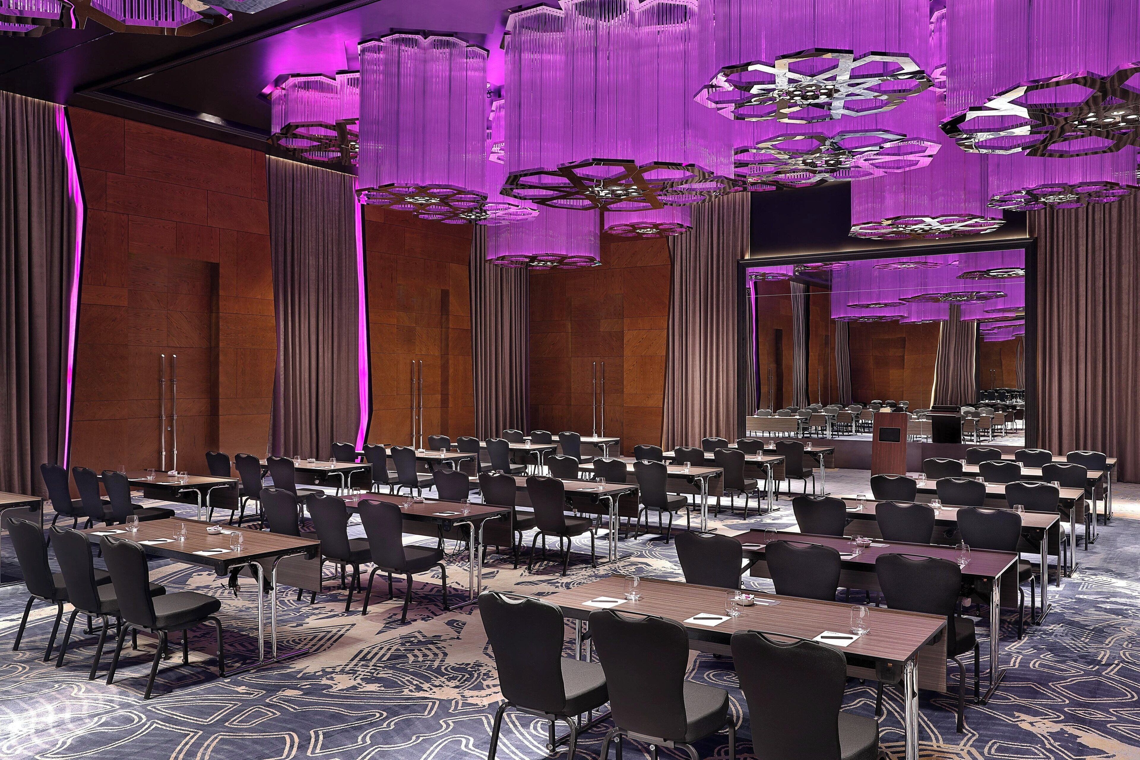 A conference room with rows of tables and chairs, a podium, and a large chandelier.