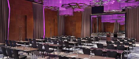 A conference room with rows of tables and chairs, a podium, and a large chandelier.