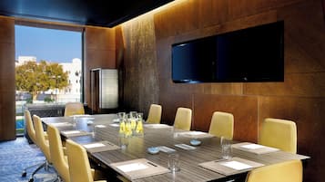 A conference room with a long table, yellow chairs, a flat-screen TV, and a view of buildings outside.