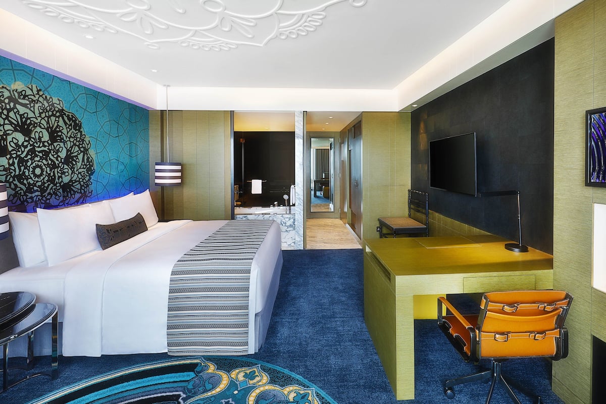A modern hotel room with a large bed, a desk, a television, and a suitcase.