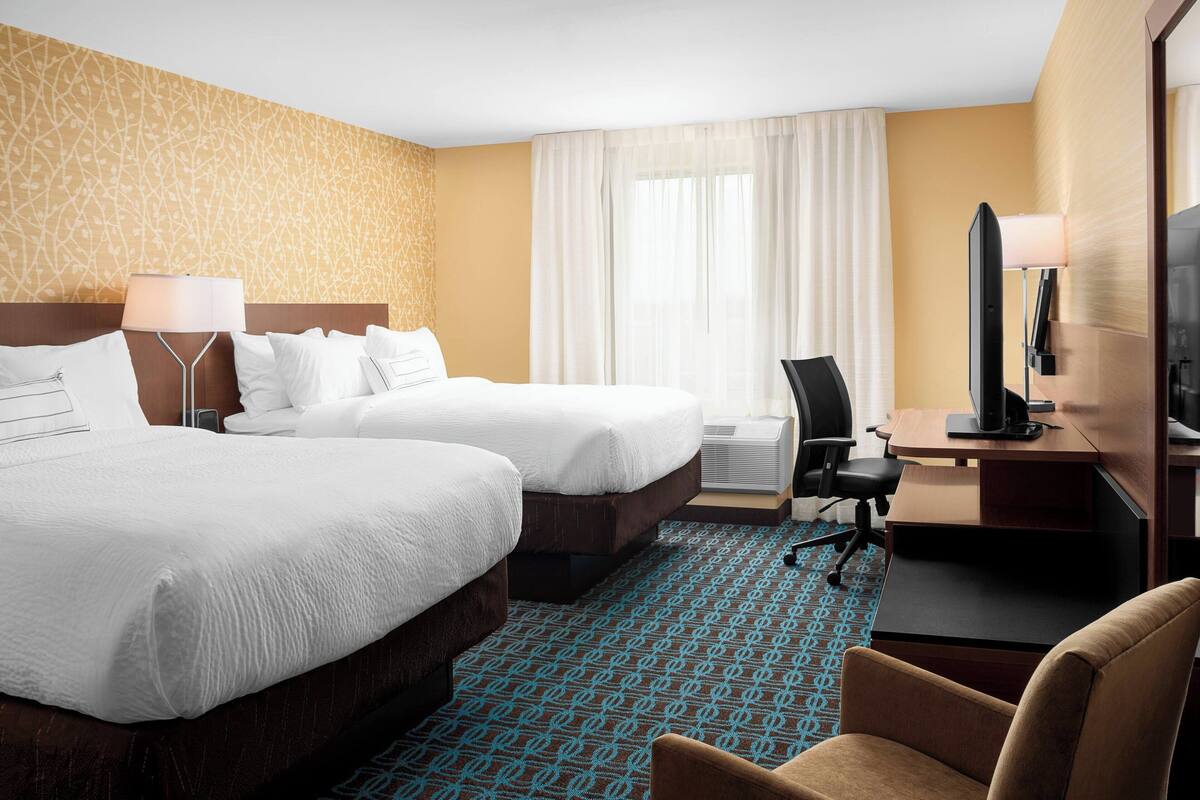 Une chambre d’hôtel avec deux lits, un bureau, une chaise, une télévision et une fenêtre avec des rideaux.
