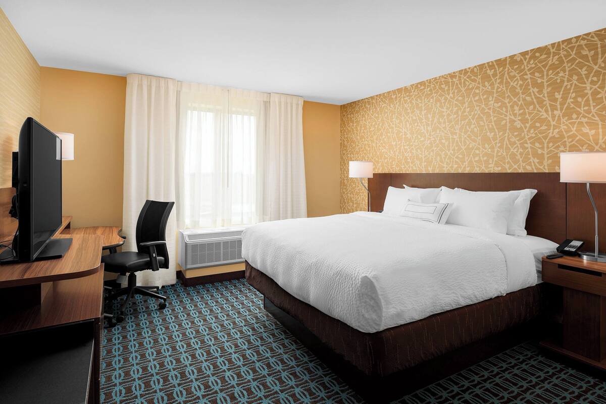 Une chambre d’hôtel équipée d’un lit, d’un bureau, d’une chaise, d’une télévision et d’une moquette à motifs.